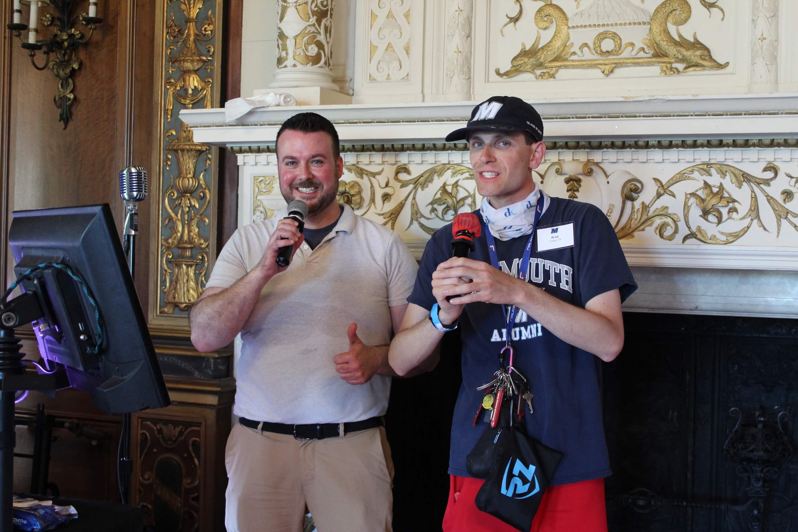 Two men speaking into microphones by a sound system in the Great Hall