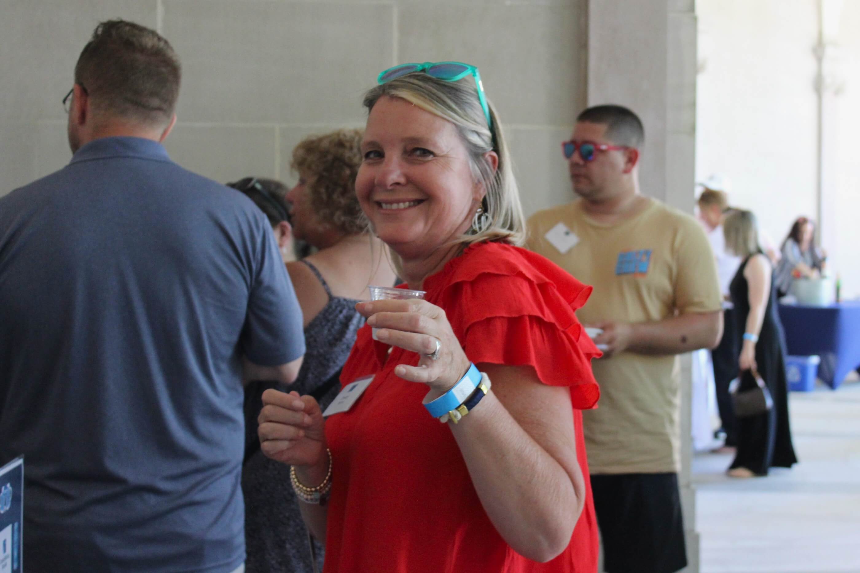 Woman in red dress and green sunglasses posing for a shot holding up her tasting glass