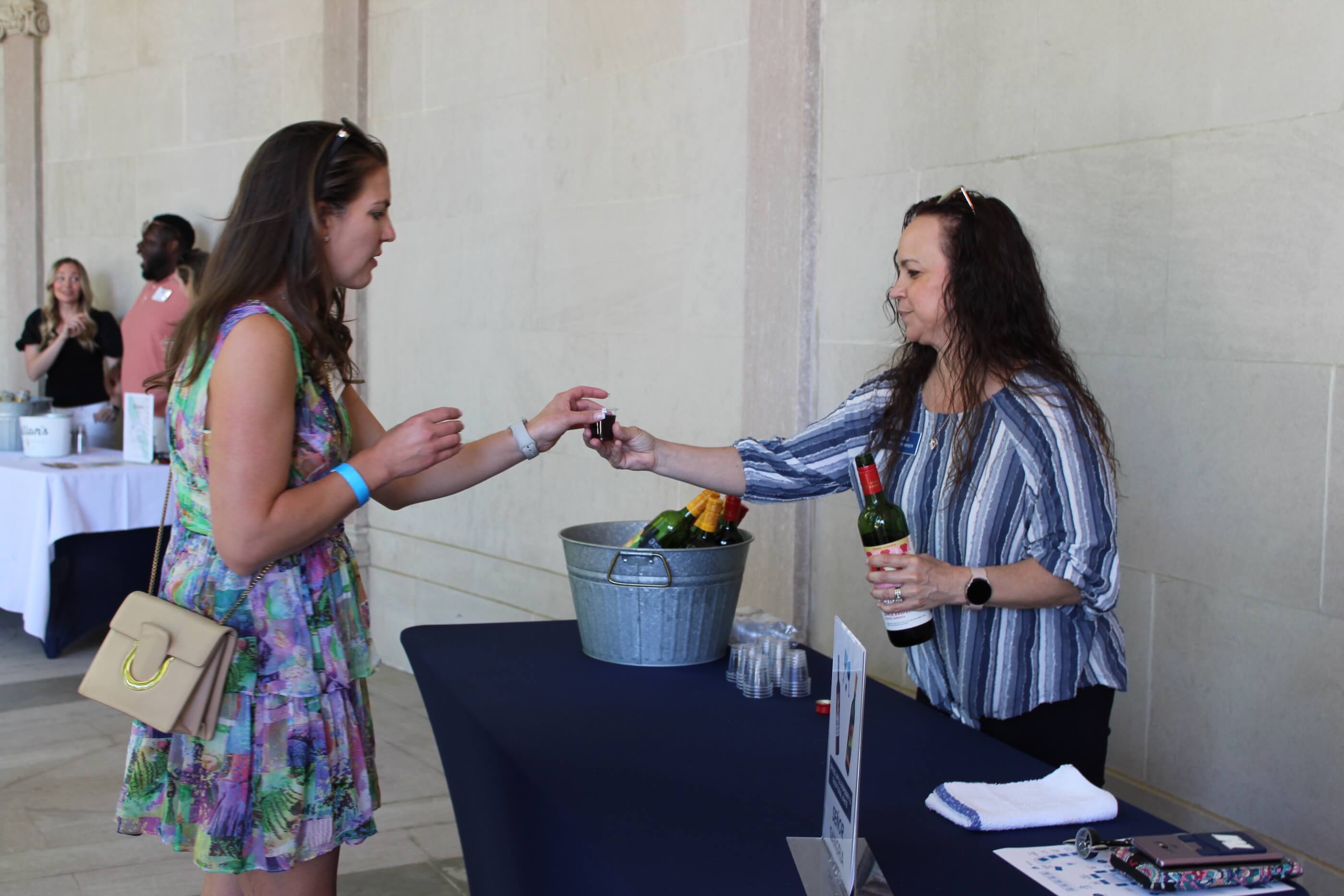 Woman accepting a tasting glass filled with red wine from a volunteer at a winery table