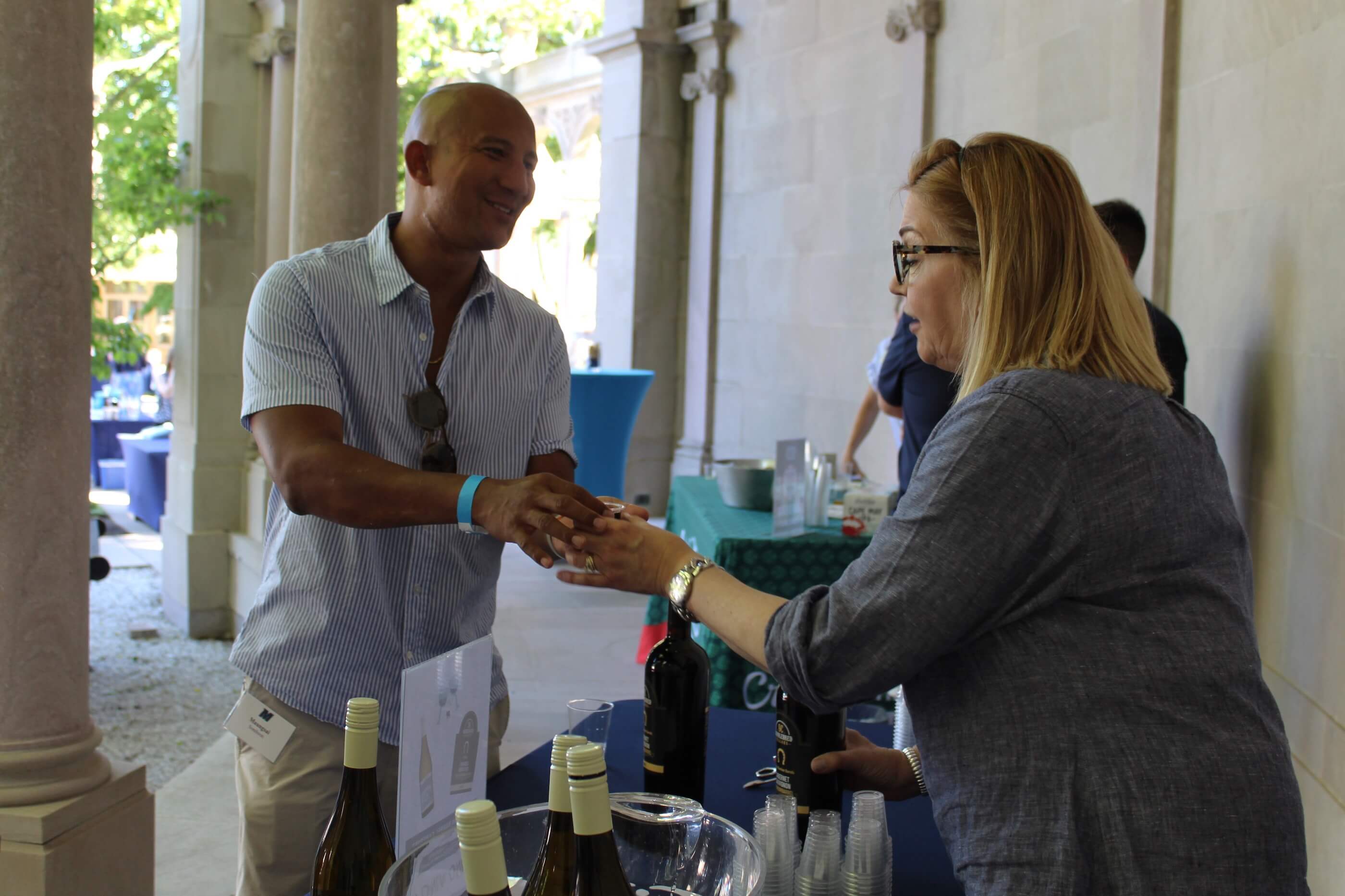 Man smiling as he takes his drinking glass from the volunteer handing it back to him at a winery table.