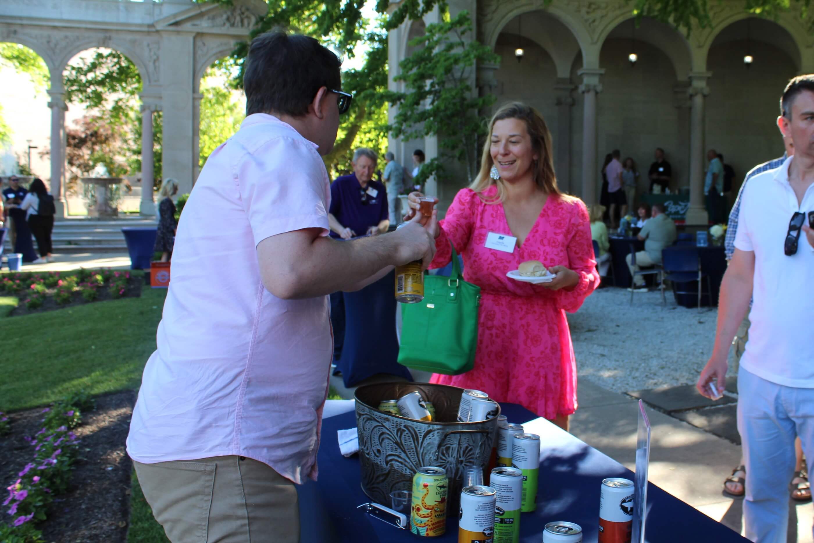 A volunteer hands back a tasting glass with beer to an attendee, with event goers talking among themselves in the background