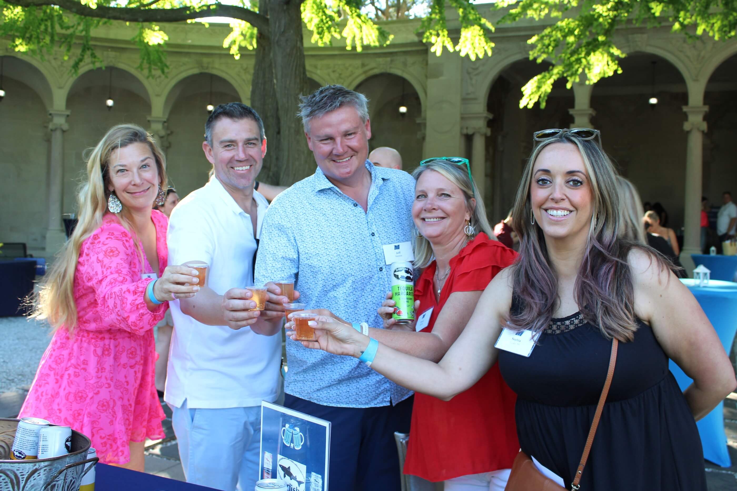 Five attendees posing for a group shot while tapping their glasses together, each glass filled with a magarita