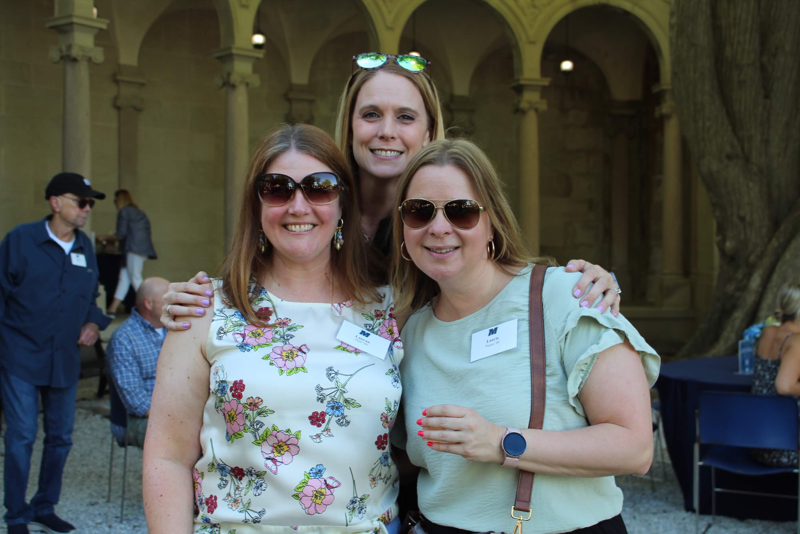 Three people posing for a group shot, one holding her tasting glass, with the columns of Erlanger Gardens in the background