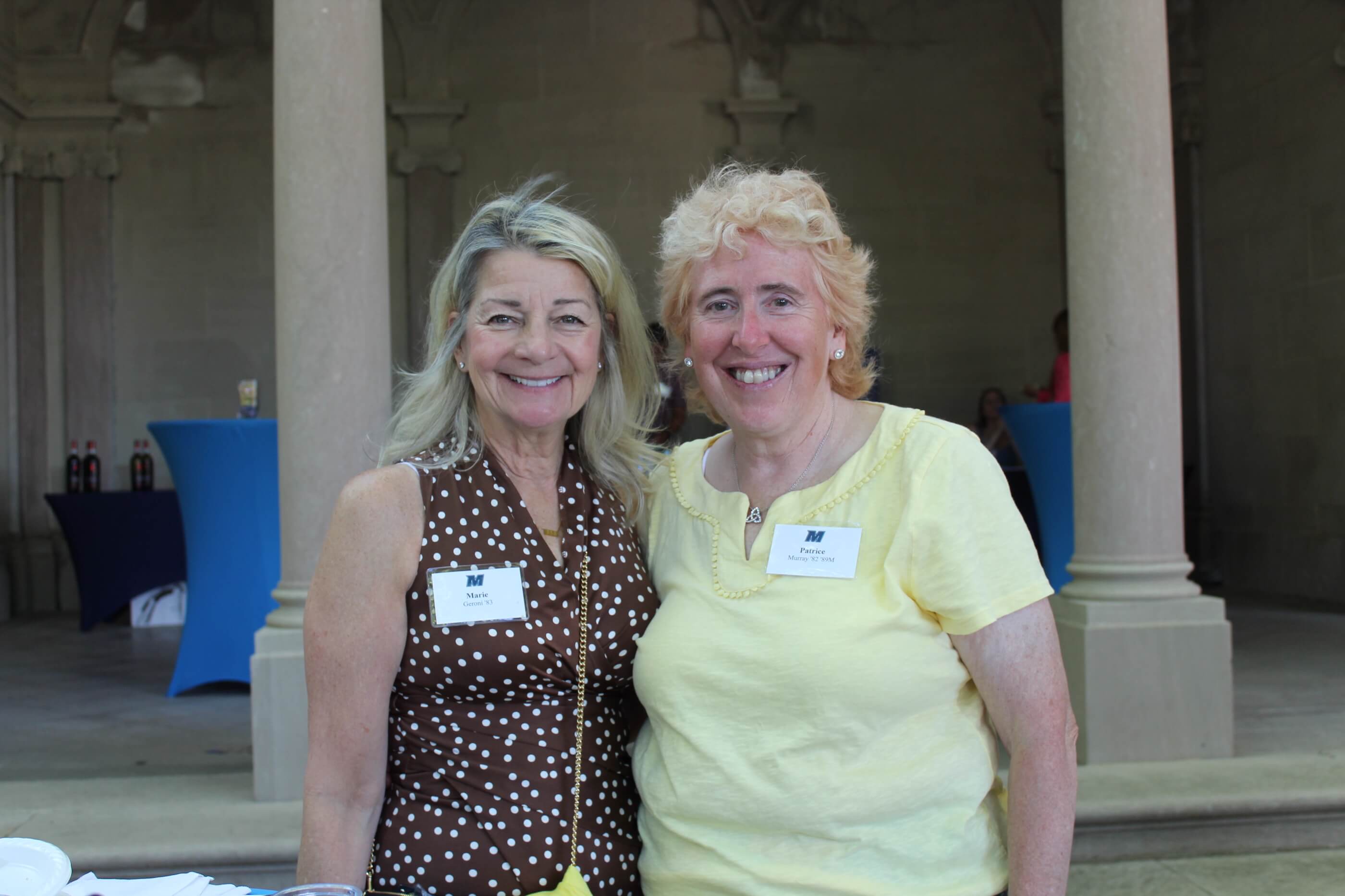 Two women smiling for the camera, with event tables and stone columns behind them