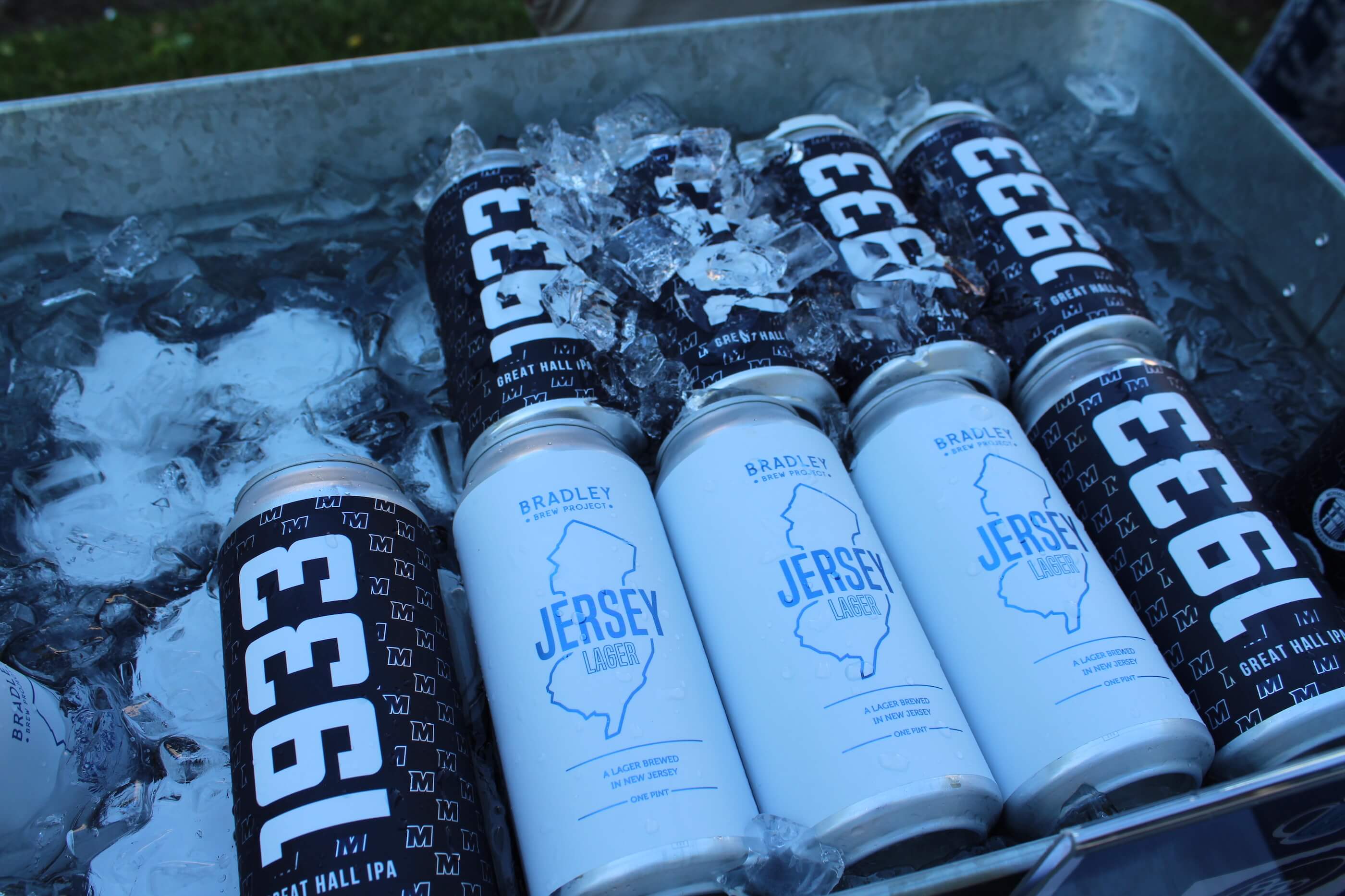 Photos of two canned beers. The first is 1933, an IPA celebrating Monmouth Universty's history (labeled a Great Hall IPA). The other is a lager called Jersey Lager, from Bradley Brew Project