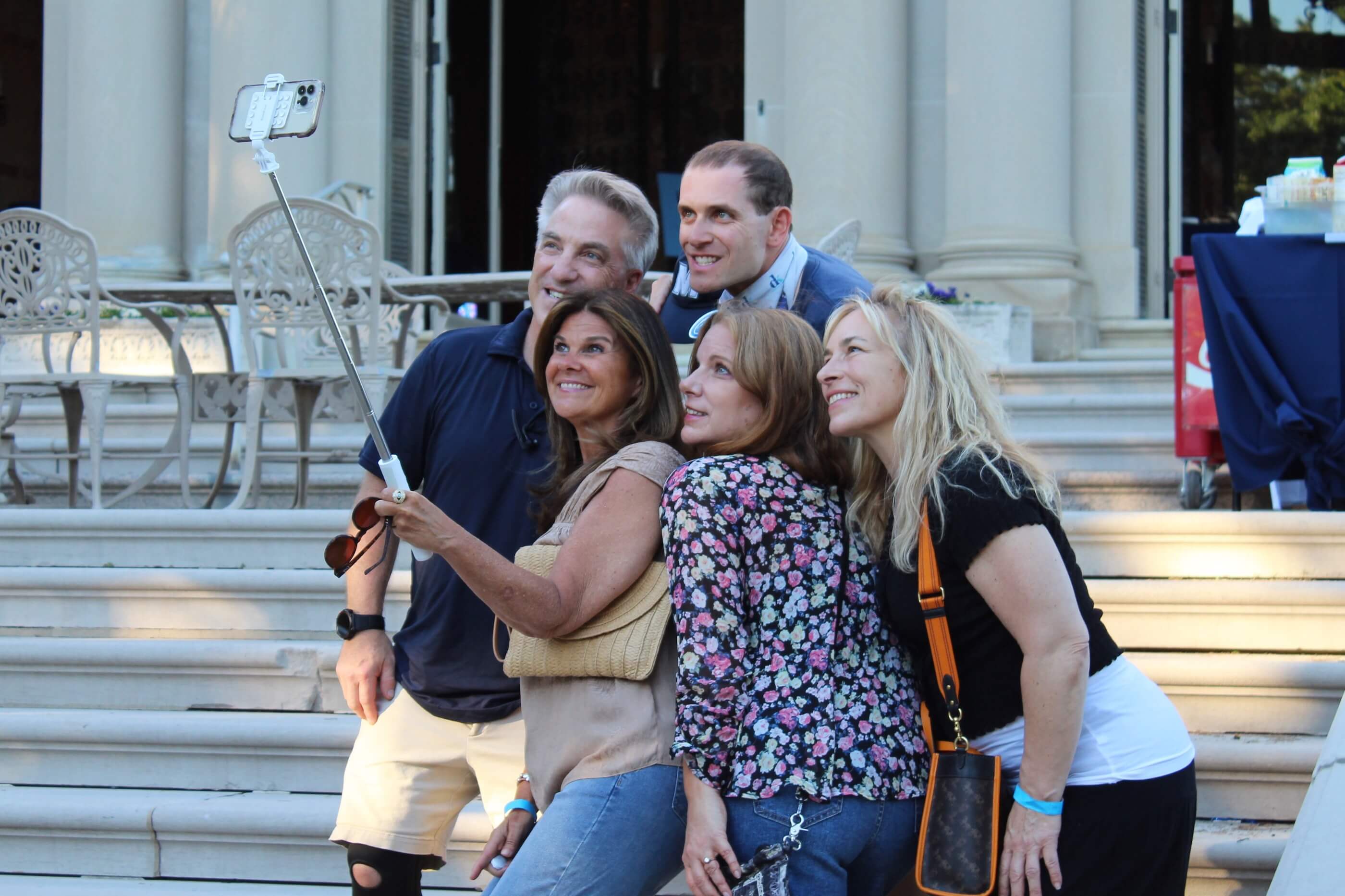 Five people using a selfie stick to take a photo of themselves on the steps of the Great Hall near Erlanger Gardens