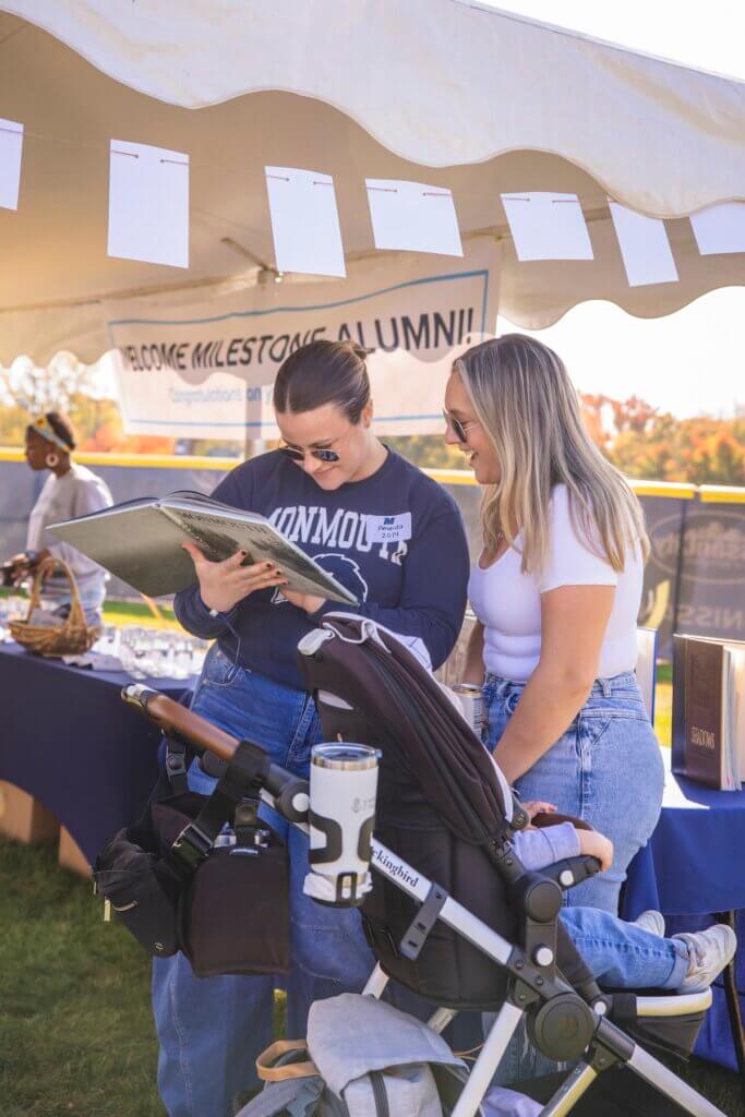 Two alumnae look at a yearbook under a tent