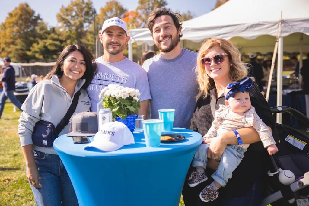 Four adults, one holding a baby, smiling for the camera in front of a high-top table