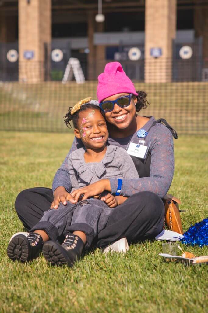 Mother with child sitting on her lap, both on the grass outside the stadium