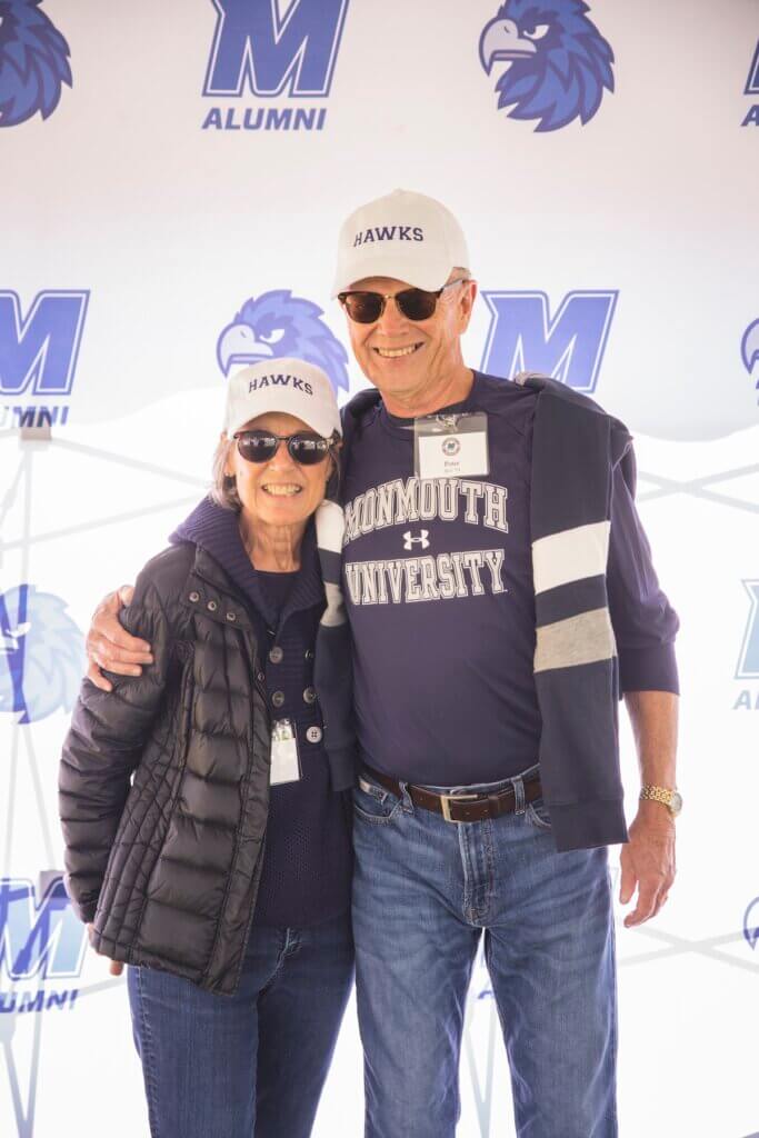 Man and woman in front of a step and repeat banner featuring monmouth iconography