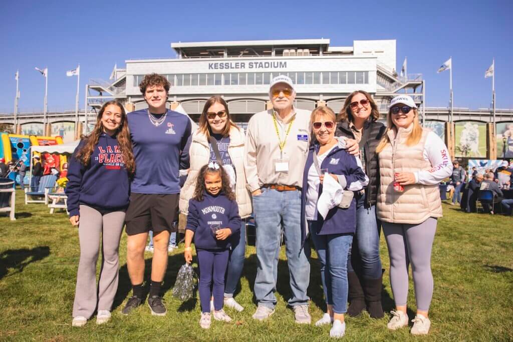 Family photo with kids and adults in monmouth gear, posing outside stadium