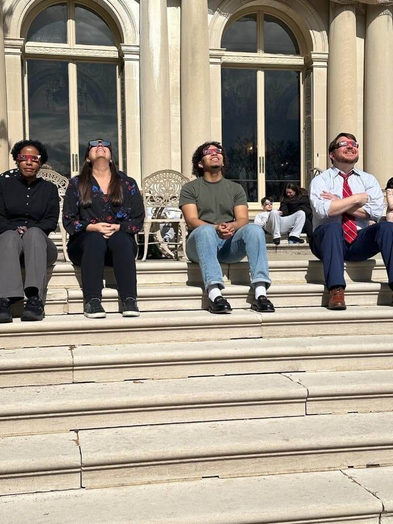 Four people on steps wearing glasses, looking at a solar eclipse