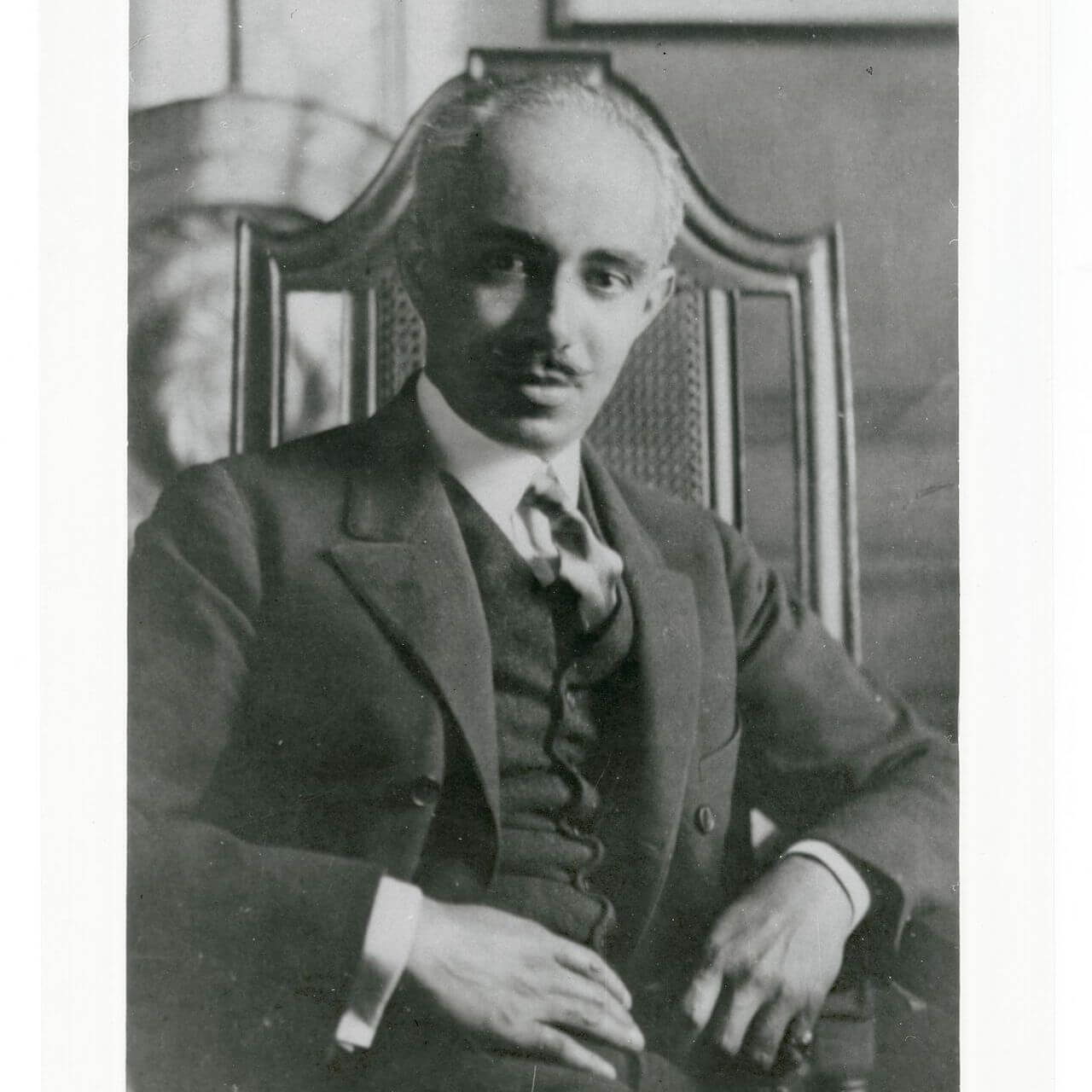 Old photograph of Julian Abele in a full suit, sitting in a wooden chair