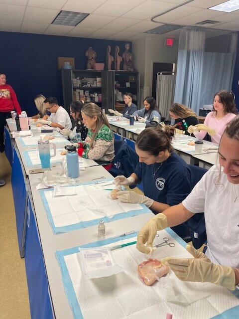 Students at tables practicing surturing on meat.