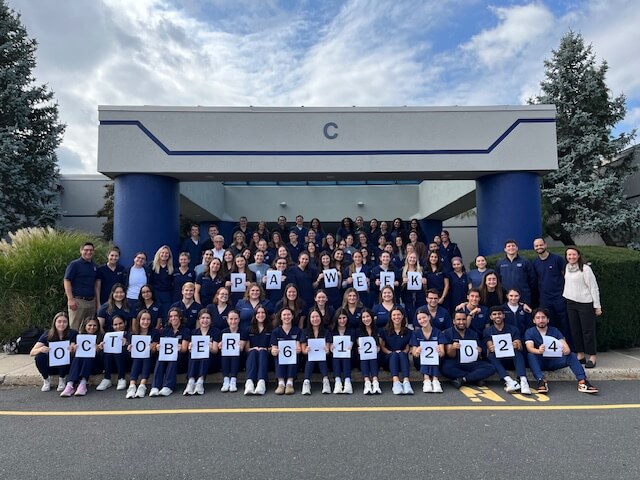 Group of students outside building holding letter cards that spell out PA Week October 6-12, 2024