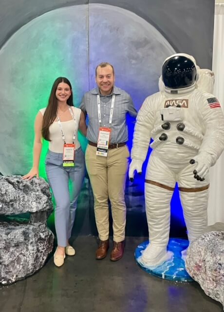 Man and woman wearing conference badges, standing next to a statue of a NASA astronaut.