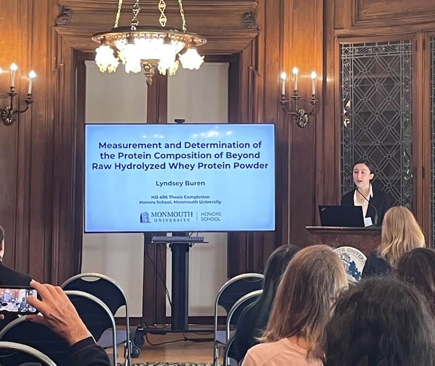 Woman speaking in hall during presentation. Title: Measurement and Determination of the Protein Composition of Beyond Raw Hydrolyzed Whey Protein Powder