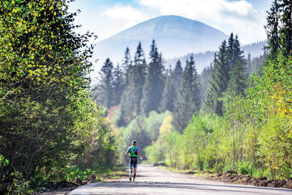 A triathlete running along a woody road with Mount Hoverla in the background