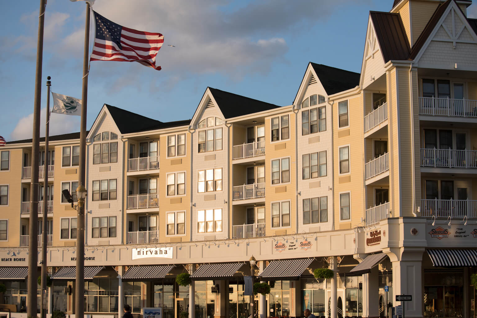 Photo of all the shops in Pier Village, along with apartment buildings above them. Flags for United States of America and Long Branch fly in the background.