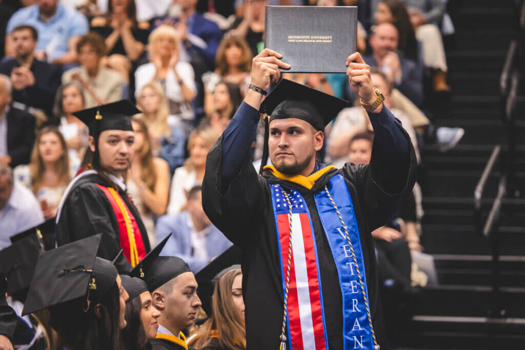 Student veteran holding diploma at commencement and wearing veteran stole.