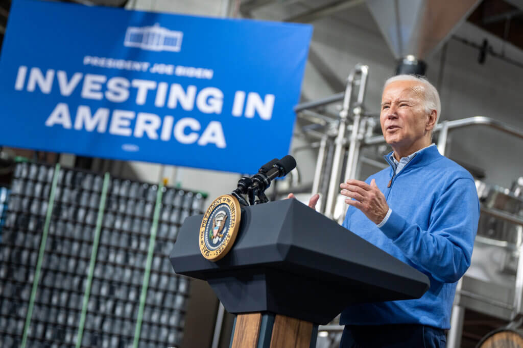 Image of President Biden at podium with sign in background that says "Investing in America"