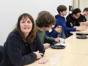 1 woman high school teacher sitting alongside a group of male students eating lunch