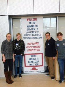 1 female MRHS teacher and 3 male students next to the HSPC banner (Welcome to the Monmouth University Dept of Computer Science & Software Engineering High School Programming Competition - Where Monmouth Hawks Code Together)