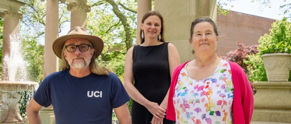 Three professors pose by a fountain in a garden