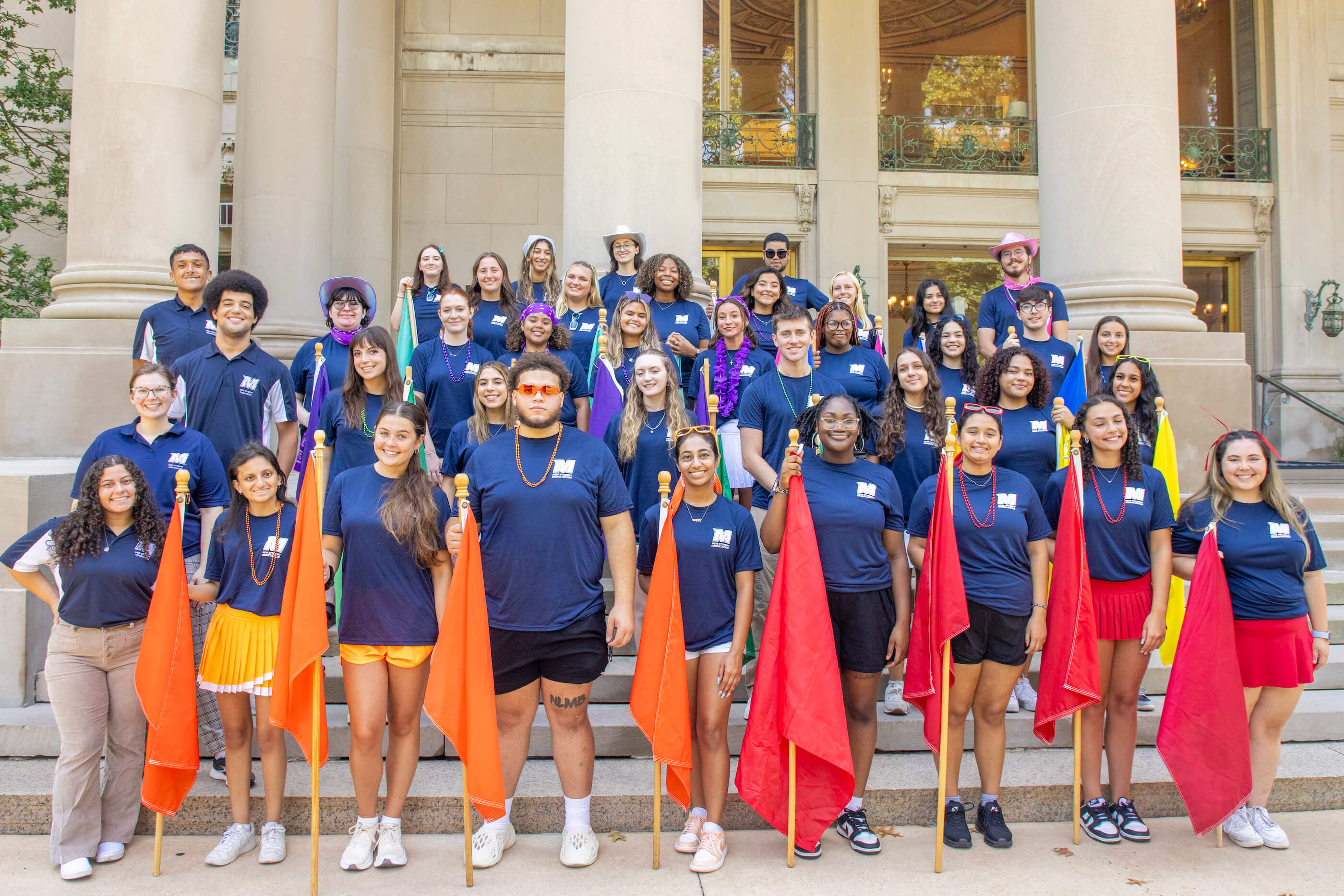 Orientation helpers on the steps of the great hall, holding orange and red flags at the front.