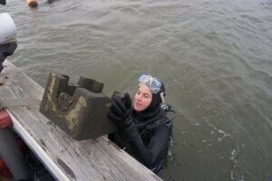 UCI Marine Biology Technician Amanda Boddy stands in the water while being handed an oyster castle block from a vessel.