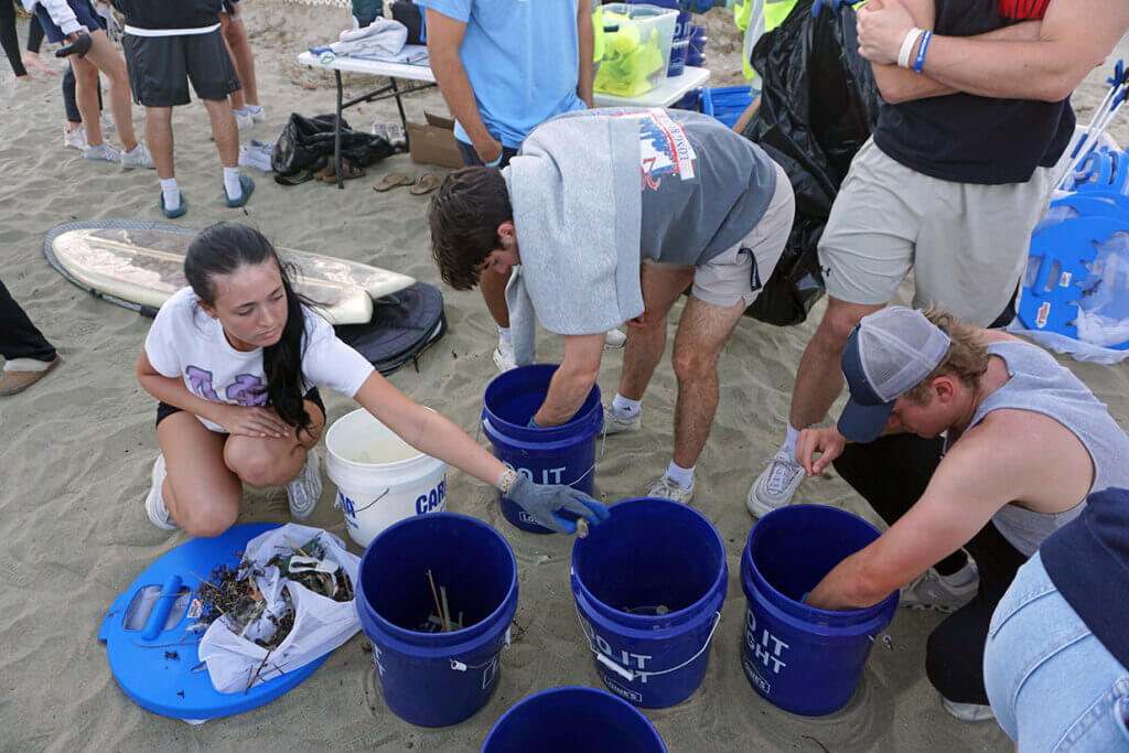 Students placing trash in buckets on the beach